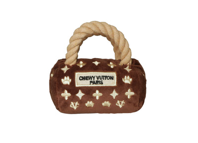 Plush luxury dog handbag toy in brown velvet with rope handles and embroidered gold icons, featuring a “Chewy Vutton Paris” label. Soft squeaky designer-style chew toy for pets.