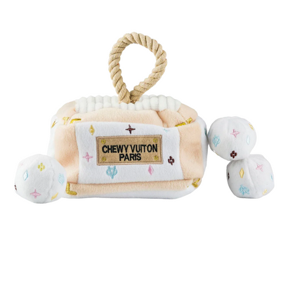 Plush interactive dog toy shaped like a designer-style handbag with a beige and white body, rope handle, and “Chewy Vuiton Paris” label, including three matching plush balls for hide-and-seek play.