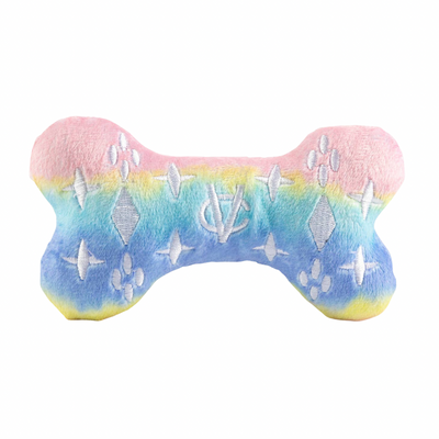 Pastel rainbow plush dog bone toy in pink, blue, and yellow gradient with white embroidered icons and a “Chewy Vuiton Paris” label. Soft luxury squeaky chew toy for pets.
