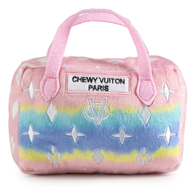 Plush dog toy shaped like a designer handbag with pink handles and a pastel rainbow gradient featuring embroidered icons and a “Chewy Vuiton Paris” label. Soft luxury squeaky chew toy for pets.
