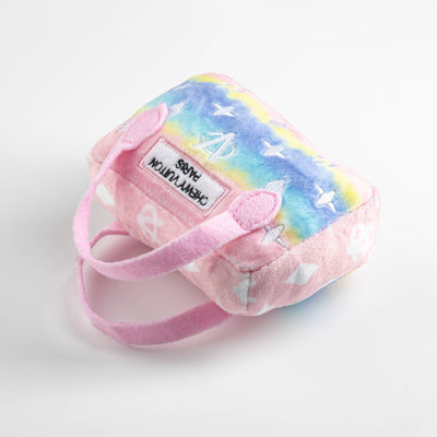 Plush dog toy shaped like a designer handbag with pink handles and a pastel rainbow gradient featuring embroidered icons and a “Chewy Vuiton Paris” label. Soft luxury squeaky chew toy for pets.