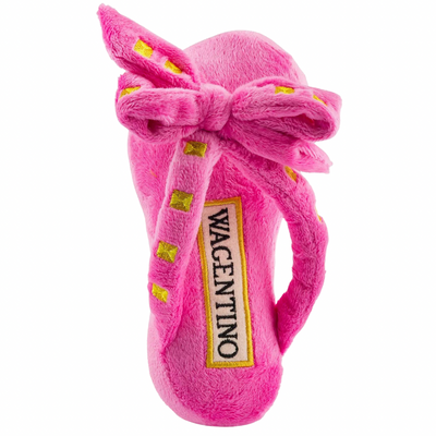 Plush dog toy shaped like a pink designer sandal with a large bow, gold stud details, and “Wagentino” embroidered on the footbed.