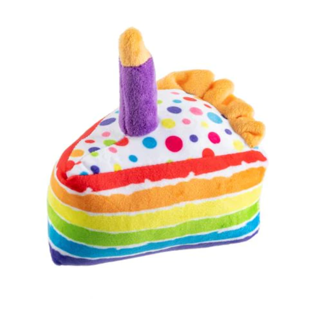 Plush dog toy shaped like a slice of rainbow birthday cake with colorful polka dot frosting and a purple candle on top. Soft squeaky celebration toy for pets.