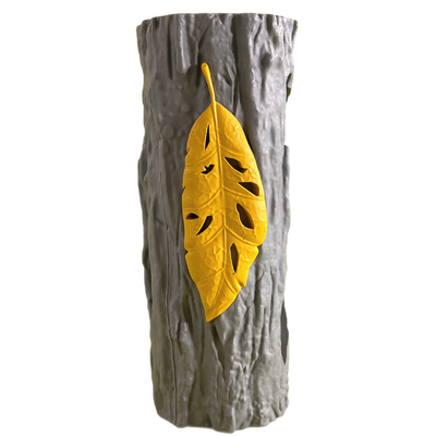 Gray rubber dog chew toy shaped like a tree trunk with textured bark and a raised yellow leaf design. Durable interactive chew toy for pets.