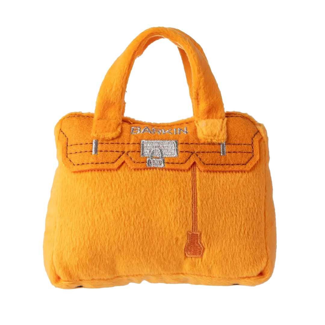 Plush dog toy shaped like a handbag with soft handles and embroidered text “Rich Bitch” on the front. Available in pink and orange colors. Luxury squeaky chew toy for pets.