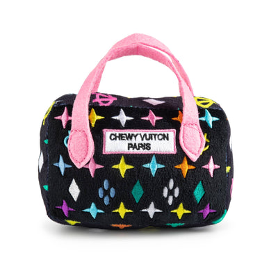 Plush dog toy shaped like a designer handbag with a black base, colorful embroidered icons, and pink handles featuring a “Chewy Vuiton Paris” label. Luxury squeaky chew toy for pets.