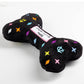 Black plush dog bone toy with colorful embroidered designer-style icons and a “Chewy Vuiton Paris” label. Soft luxury squeaky chew toy for pets.