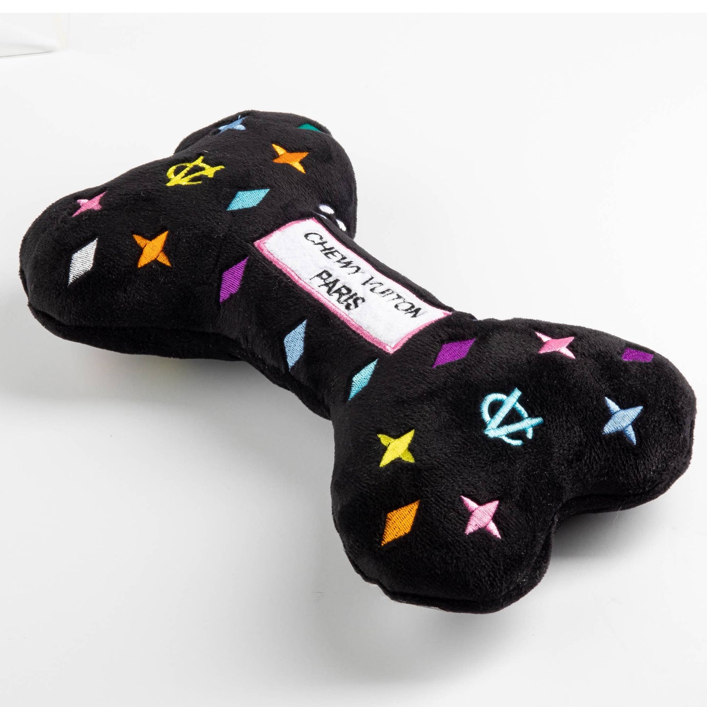 Black plush dog bone toy with colorful embroidered designer-style icons and a “Chewy Vuiton Paris” label. Soft luxury squeaky chew toy for pets.