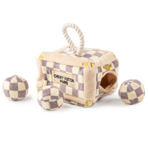 Plush interactive dog toy shaped like a designer-style trunk with a beige and lavender check pattern, rope handle, and “Chewy Vuiton Paris” label, including four matching plush balls to hide and retrieve.