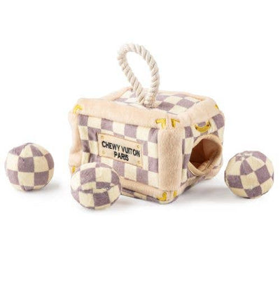 Plush interactive dog toy shaped like a designer-style trunk with a beige and lavender check pattern, rope handle, and “Chewy Vuiton Paris” label, including four matching plush balls to hide and retrieve.