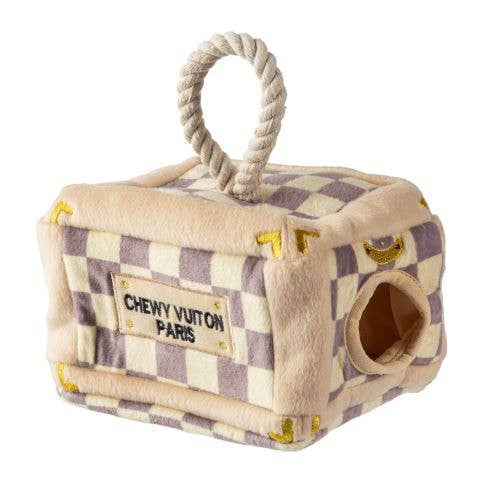 Plush interactive dog toy shaped like a designer-style trunk with a beige and lavender check pattern, rope handle, and “Chewy Vuiton Paris” label, including four matching plush balls to hide and retrieve.