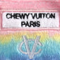Plush dog toy shaped like a designer handbag with pink handles and a pastel rainbow gradient featuring embroidered icons and a “Chewy Vuiton Paris” label. Soft luxury squeaky chew toy for pets.