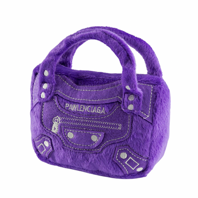 Purple plush dog toy shaped like a designer handbag with stitched pocket details and “Pawlenciaga” embroidered on the front. Soft luxury squeaky chew toy for pets.