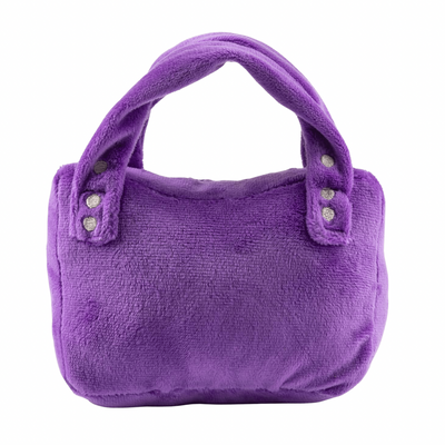 Purple plush dog toy shaped like a designer handbag with stitched pocket details and “Pawlenciaga” embroidered on the front. Soft luxury squeaky chew toy for pets.